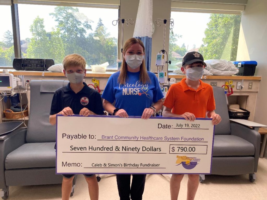 Pictured, Simon (left) and Caleb (right) present RN Melanie Cavanaugh with their donation in the Cancer Clinic at the Brant Community Healthcare System.