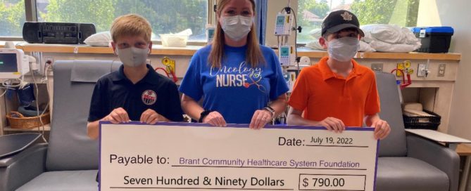 Pictured, Simon (left) and Caleb (right) present RN Melanie Cavanaugh with their donation in the Cancer Clinic at the Brant Community Healthcare System.